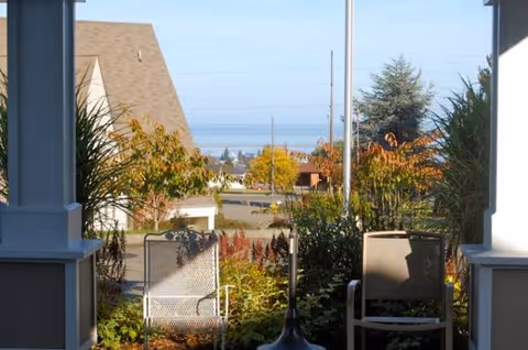 Outdoor patio with chairs, potted plants, and a distant view of the street and ocean.