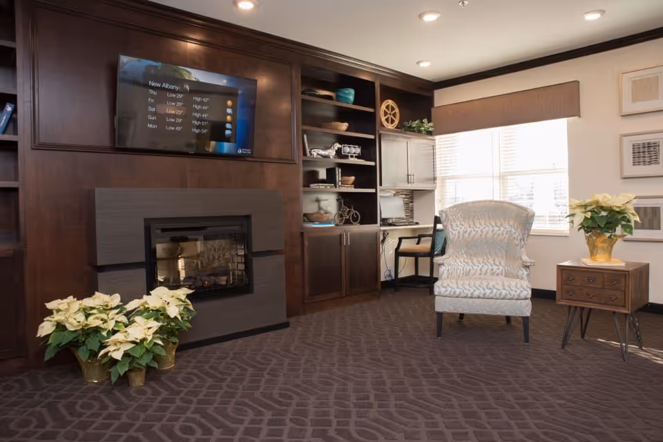 Cozy lounge area with an upholstered armchair, side table, built-in dark wood shelving and cabinets, a fireplace and a wall-mounted TV.