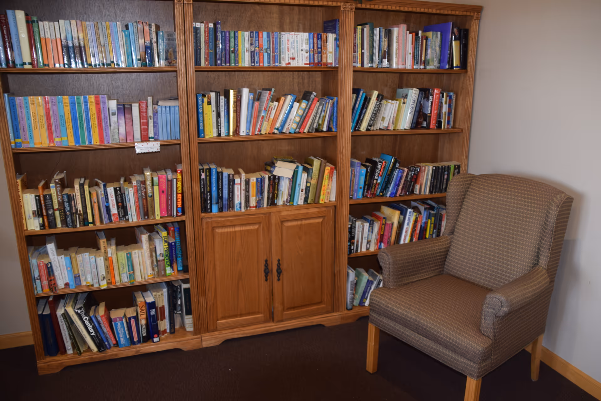 Wooden bookshelf filled with books next to a patterned upholstered armchair in a small reading nook.