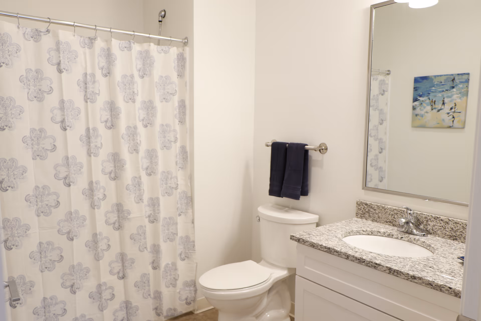 Bathroom with patterned shower curtain, toilet, granite countertop vanity, and mirror.
