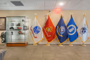 Lobby area showing five flags on stands and a glass display case with memorabilia against a beige wall.
