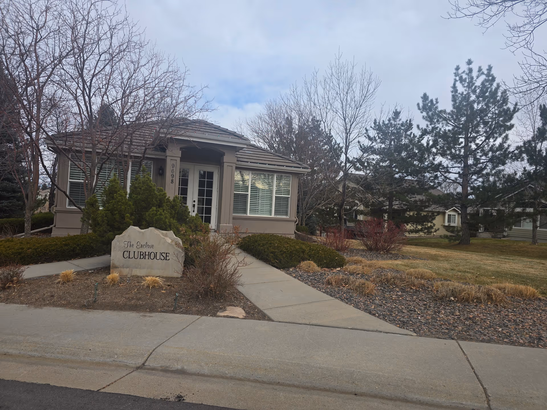 Single-story clubhouse with a stone sign reading 'The Enclave Clubhouse' in front and surrounding landscaped yard.