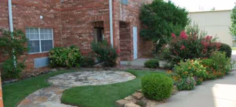Brick senior living facility entrance with landscaped shrubs and a stone walkway