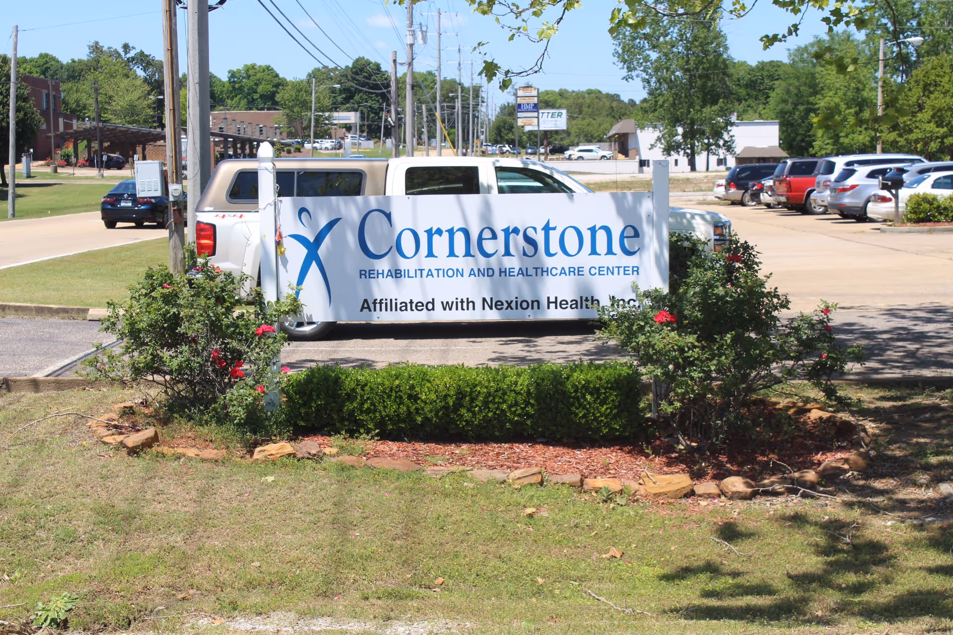 Sign for Cornerstone Rehabilitation and Healthcare Center in a landscaped front area with parked cars behind it.