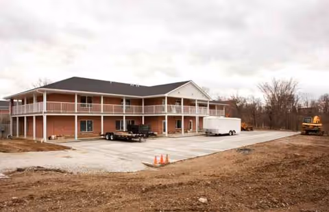 Two-story brick senior living building exterior with construction equipment and a trailer in the parking lot.