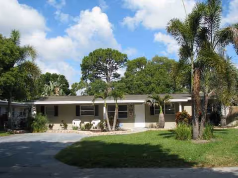 Single-story Norwood Assisted Living facility with driveway, palm trees, and a landscaped front lawn.