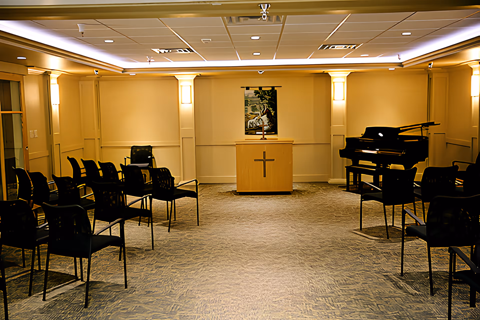 Chapel-style meeting room with rows of chairs facing a wooden lectern bearing a cross and a piano to the right.