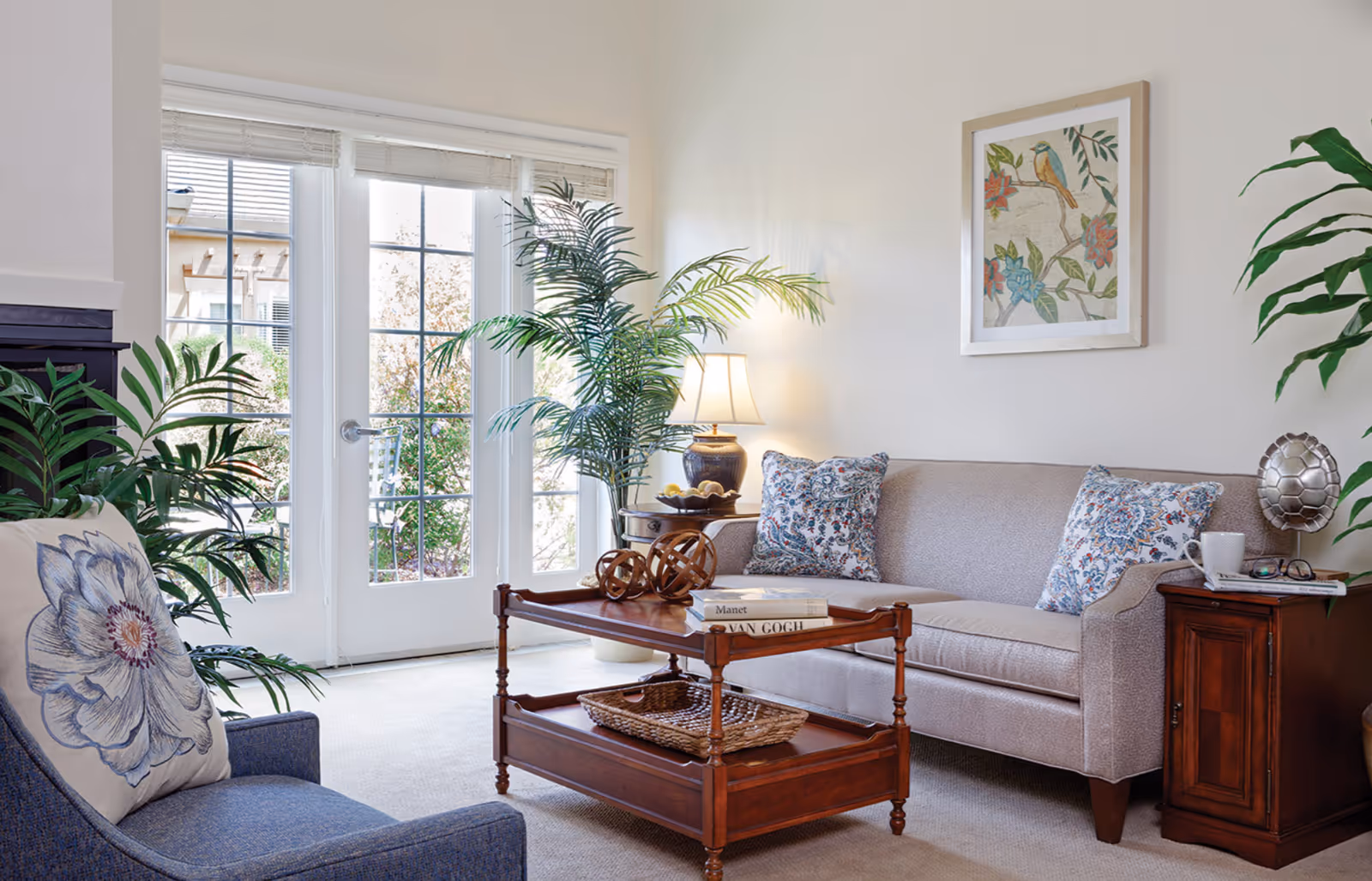 Bright living room with a sofa, armchair, wooden coffee table, potted plants, and French doors to the outside.