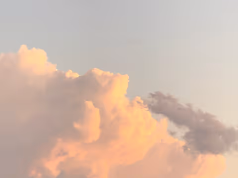 Sunlit pink and orange clouds against a pale sky at sunset.