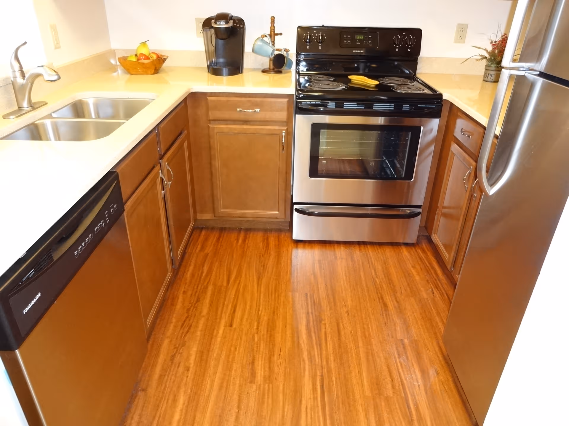 Small U-shaped kitchen with wood cabinets, stainless steel appliances, double sink and electric stove.