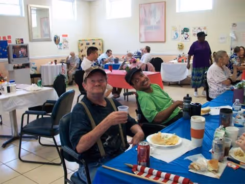 Older adults sitting at decorated tables, eating and socializing in a bright community dining room.
