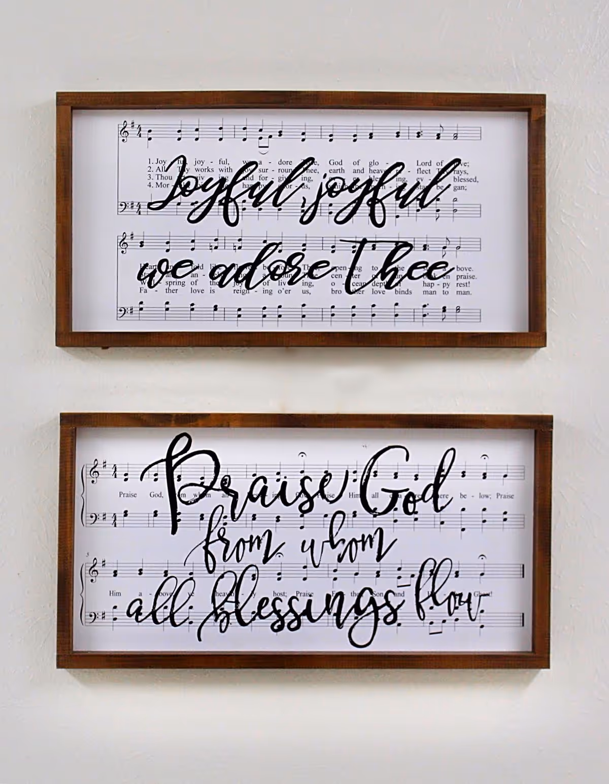 Two wooden-framed prints of sheet music with large calligraphic lyrics hanging on a white wall.
