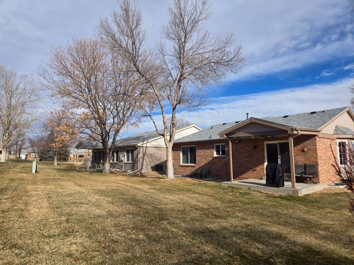 Single-story brick residential units with covered patios facing a grassy courtyard and leafless trees under a partly cloudy sky.