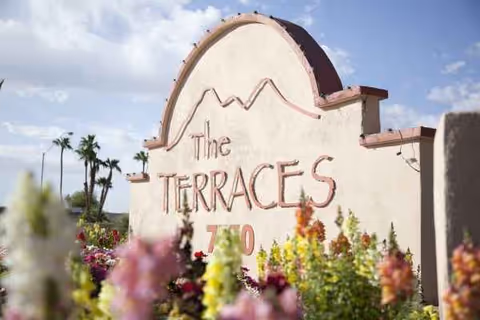 The Terraces sign on a stucco wall with colorful flowers in front.