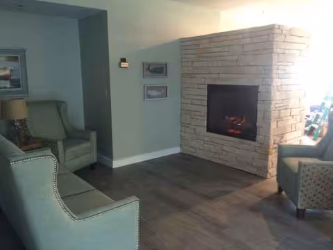 A cozy living room with a stone fireplace, blue upholstered chairs, and wall art.