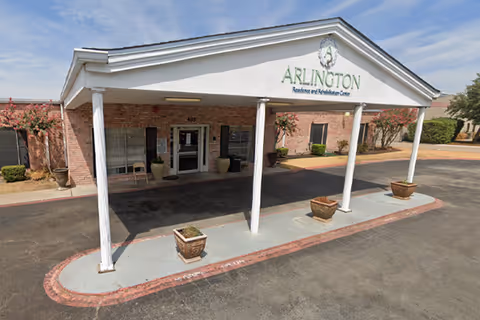 Front exterior view of Arlington Residence and Rehabilitation Center with a covered entry and potted plants.
