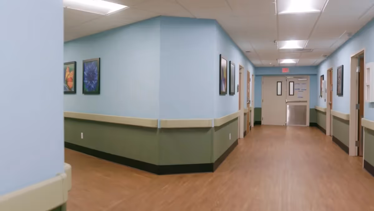 A well-lit hallway with blue walls and wooden flooring, featuring framed artwork on the walls and doors leading to various rooms.
