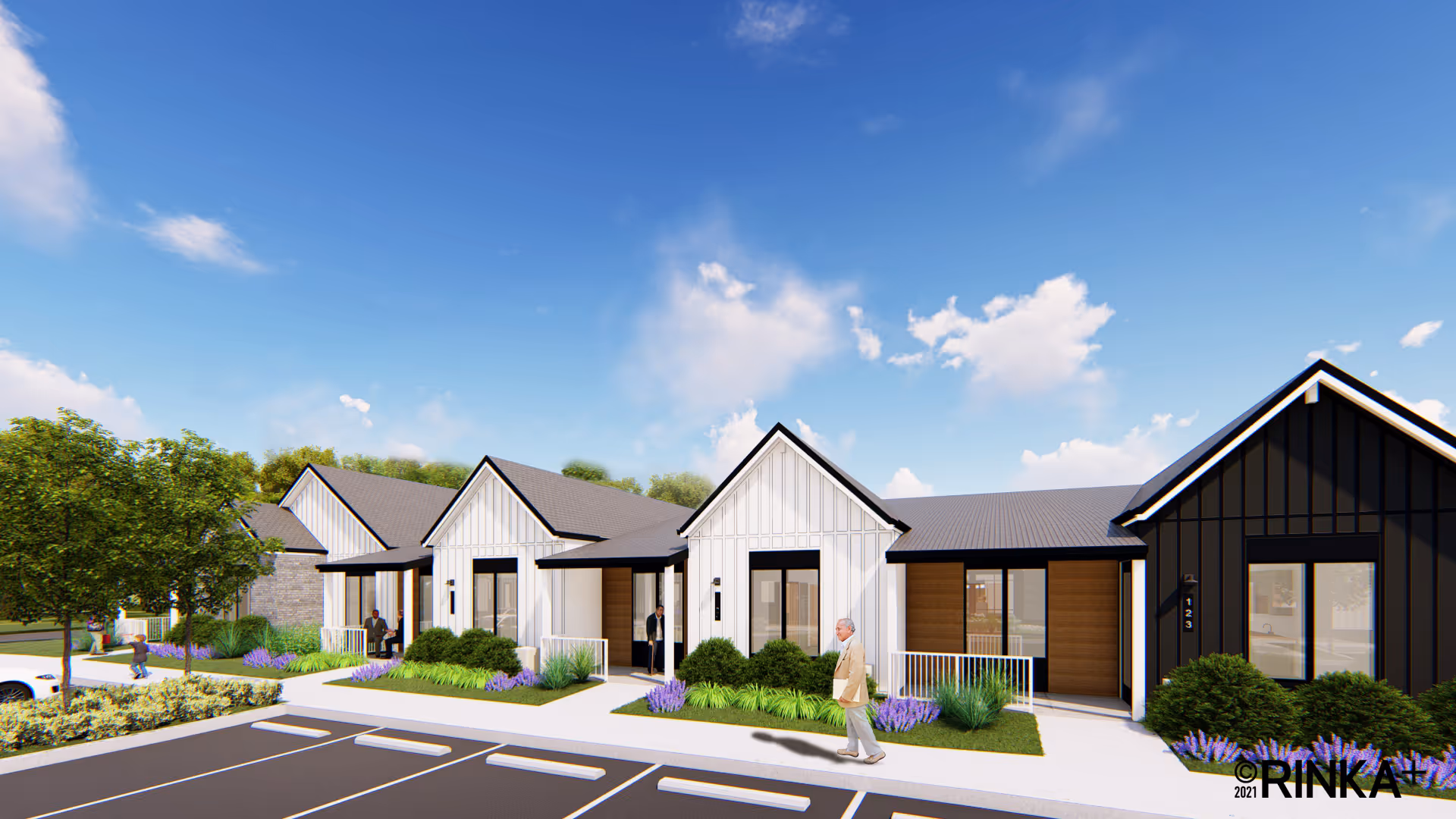 Exterior view of a modern senior living community building with multiple connected units featuring white and black siding, large windows, landscaped greenery, and a parking area in front. Several people are walking or standing near the entrances under a partly cloudy blue sky.