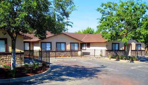 Single-story assisted living facility with a parking lot and trees in front.