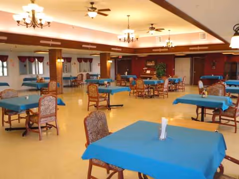Spacious dining room with blue tablecloths and cushioned chairs.