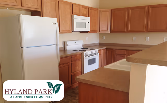 A kitchen with wooden cabinets, a white refrigerator, a white microwave mounted above a white stove, and brown countertops. The kitchen has a double sink and a partial view of a breakfast bar or counter extension.