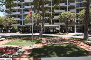 Ventura Townehouse exterior building with a flag, trees, and entry courtyard.