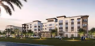 Exterior view of a modern, multi-story senior living facility named Grand Living at Naples, surrounded by green lawns, palm trees, and a few people walking and sitting outside during sunset.