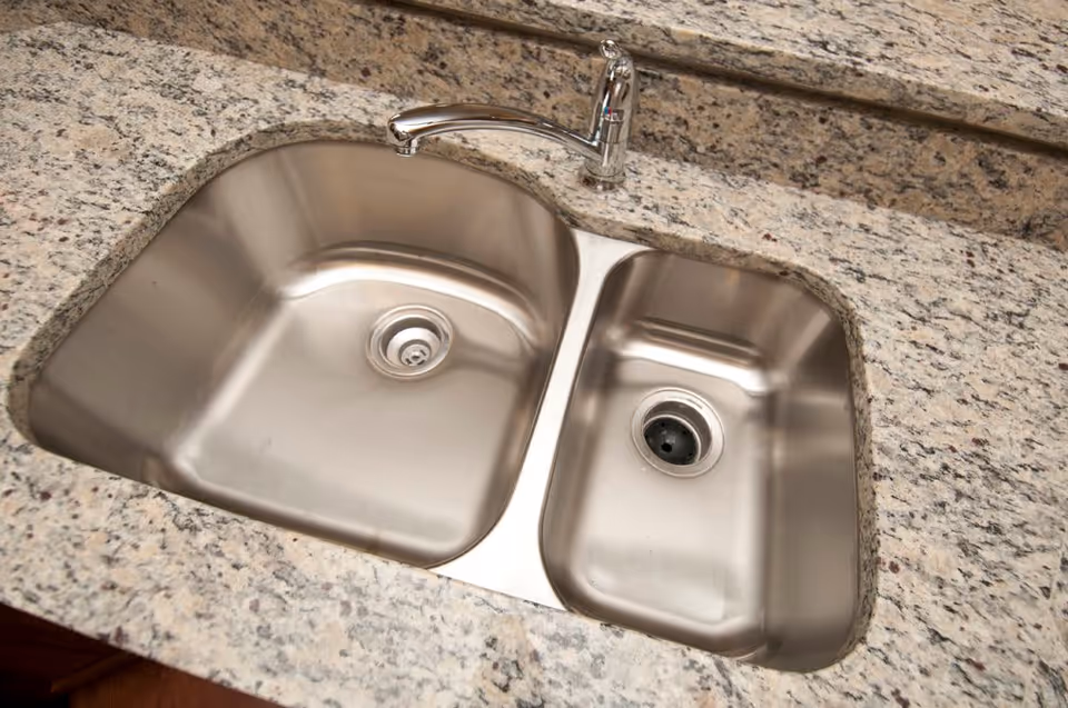 A double stainless steel kitchen sink with a single chrome faucet mounted on a speckled granite countertop.