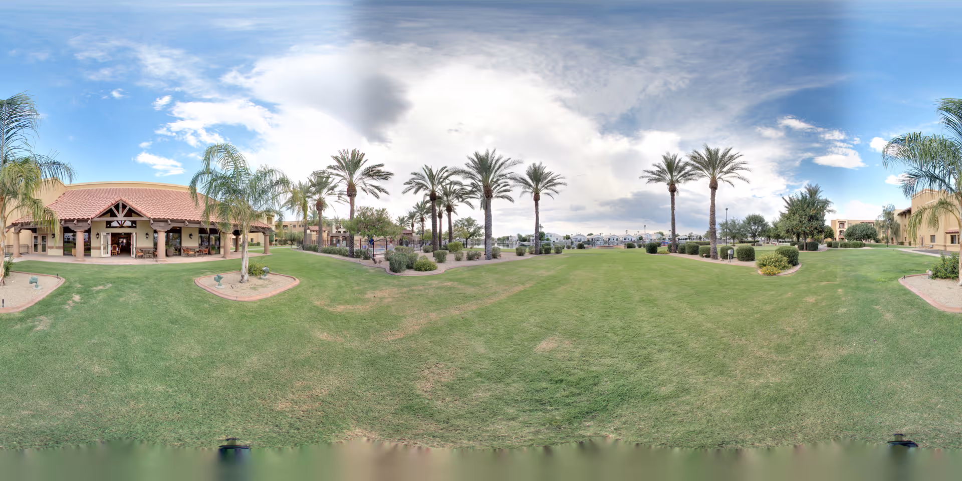 Panoramic view of a landscaped lawn with palm trees and a covered patio in front of single-story buildings.