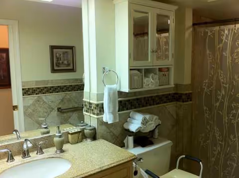Bathroom with double sink, mirror, cabinet, towels, and beige tile.