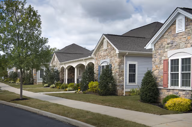 Single-story stone-faced senior living buildings with porches, landscaped lawns, and a sidewalk under a cloudy sky.