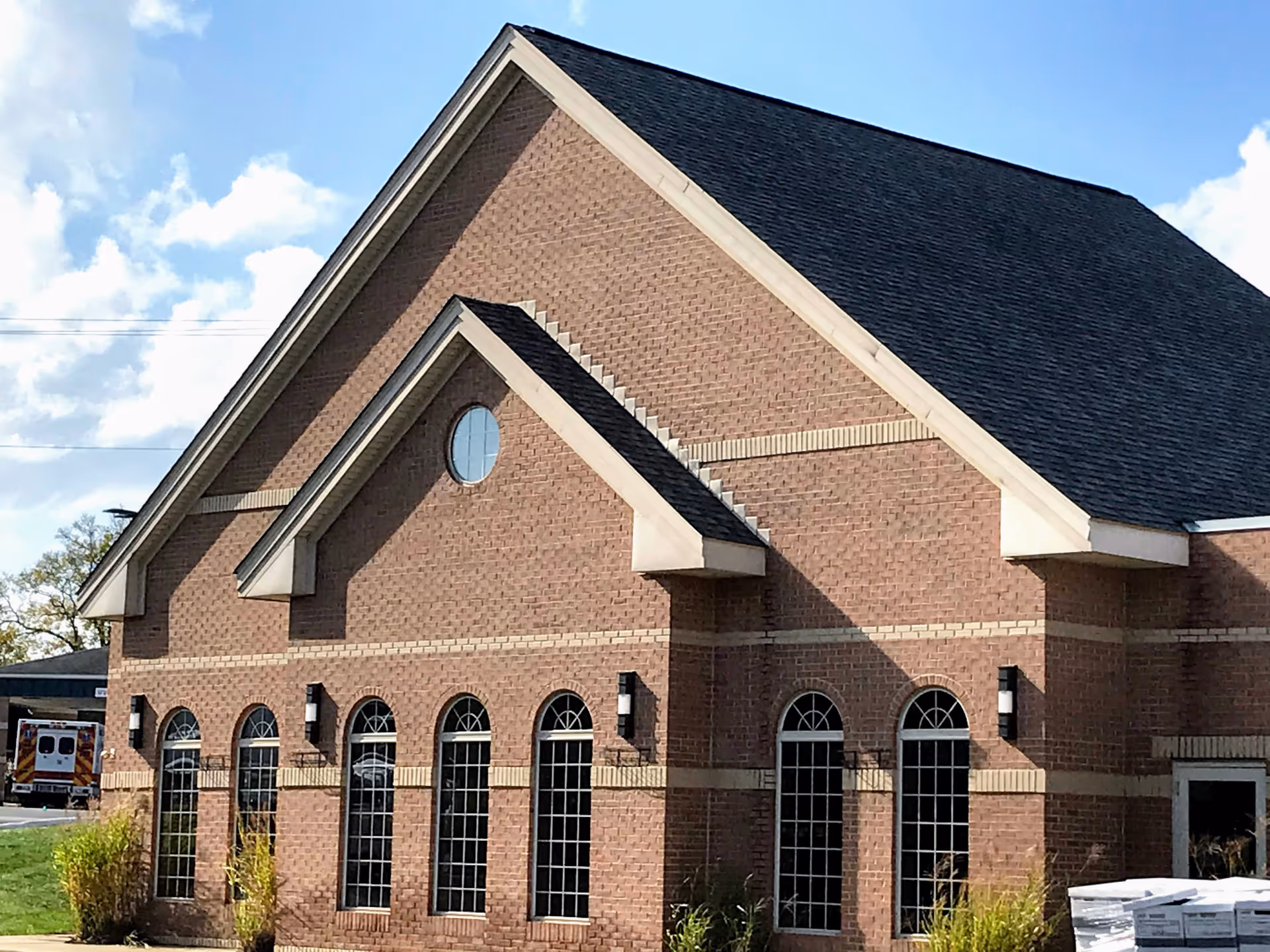 Exterior view of a brick building with a steeply pitched roof and multiple tall arched windows, under a partly cloudy sky.