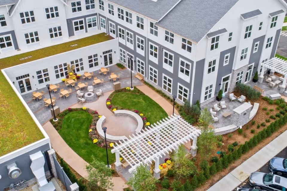 Aerial view of a landscaped central courtyard with seating areas, a pergola and firepit surrounded by a three-story senior living building.