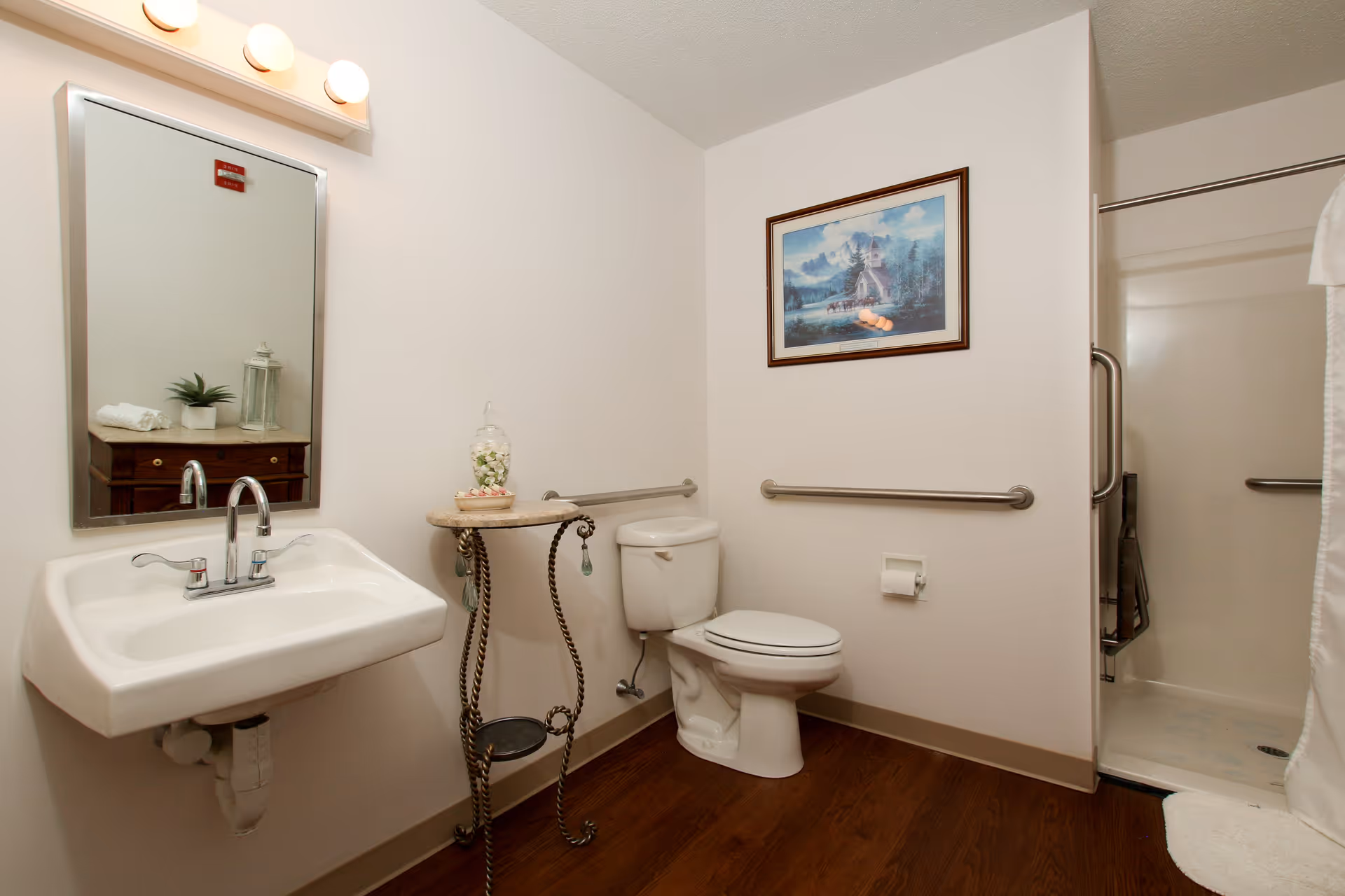 Accessible bathroom with a wall-mounted sink, toilet, grab bars, and a shower stall.