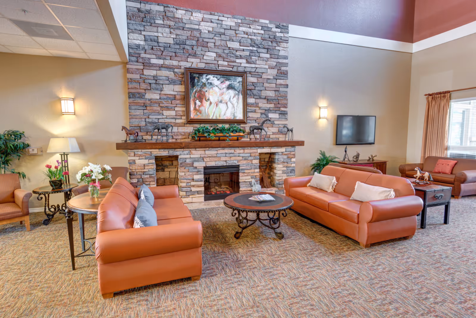 Spacious lounge with leather sofas arranged around a stone fireplace, coffee table, and wall-mounted TV.