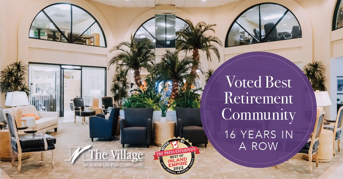Bright senior living lobby lounge with chairs, tables, large indoor palm plants, and a purple banner promoting the community.