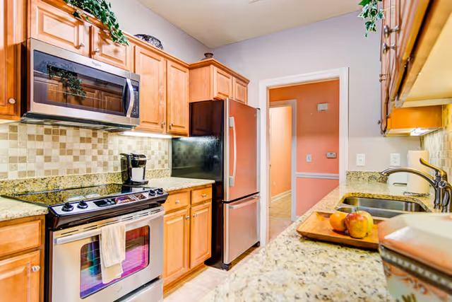 Modern kitchen with stainless steel refrigerator and oven, granite countertops, wooden cabinets, and a sink at a breakfast bar.