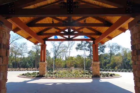 Covered wooden porte-cochere entry with stone pillars over a circular driveway and landscaped island.