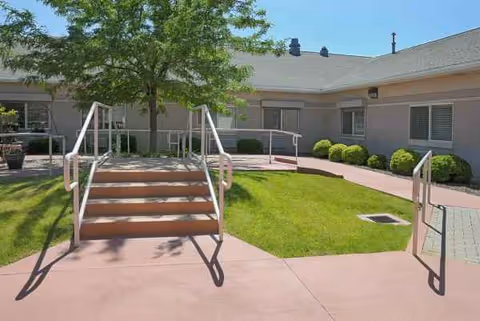 Exterior view of a senior living center courtyard with steps, a ramp, and green lawn.