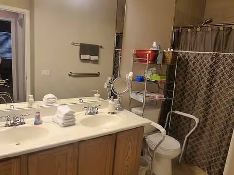 Accessible bathroom with double sinks, mirror, towels, shower curtain, and grab bars.
