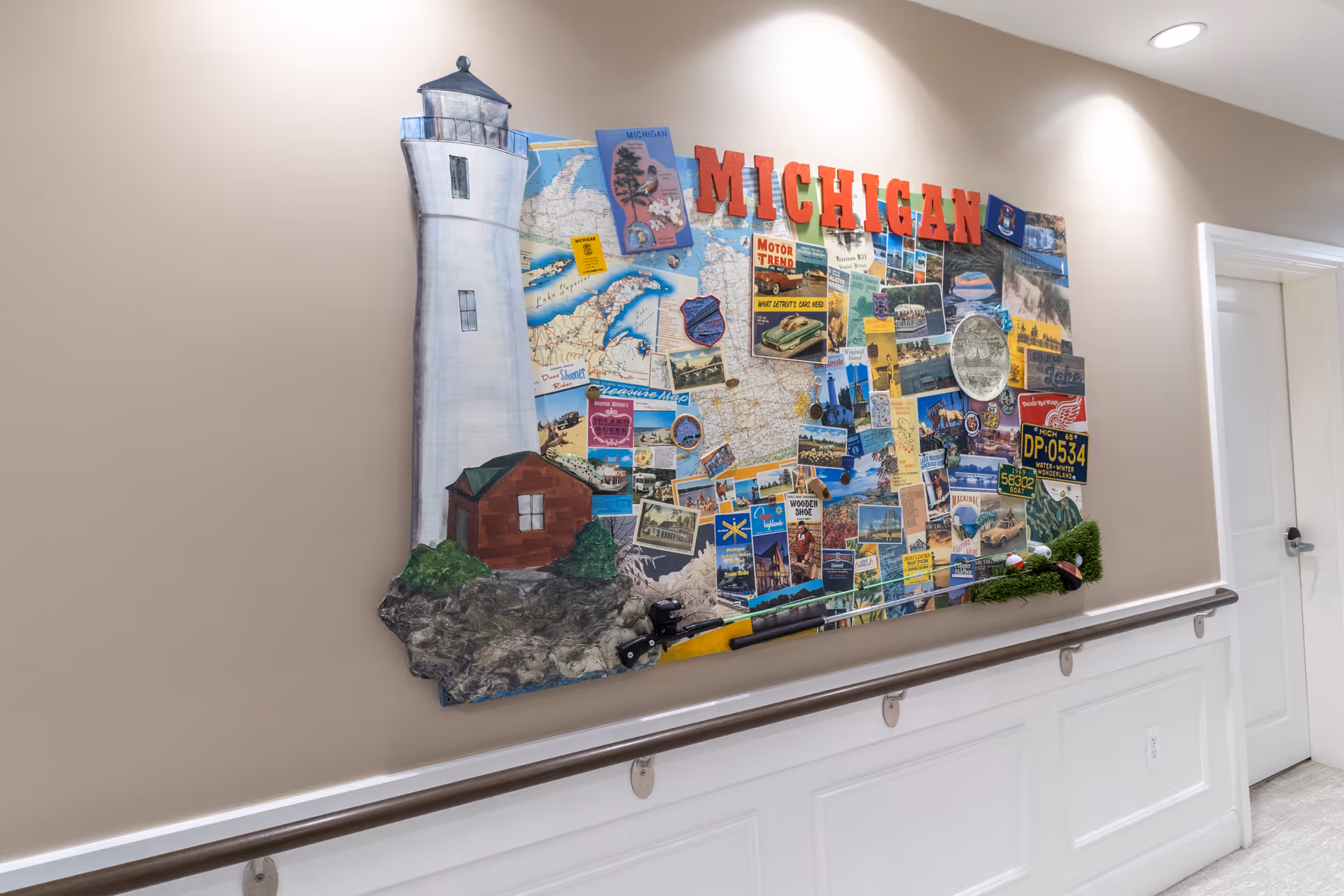 Wall-mounted Michigan-themed collage featuring a lighthouse and postcards above a handrail in a well-lit interior corridor.