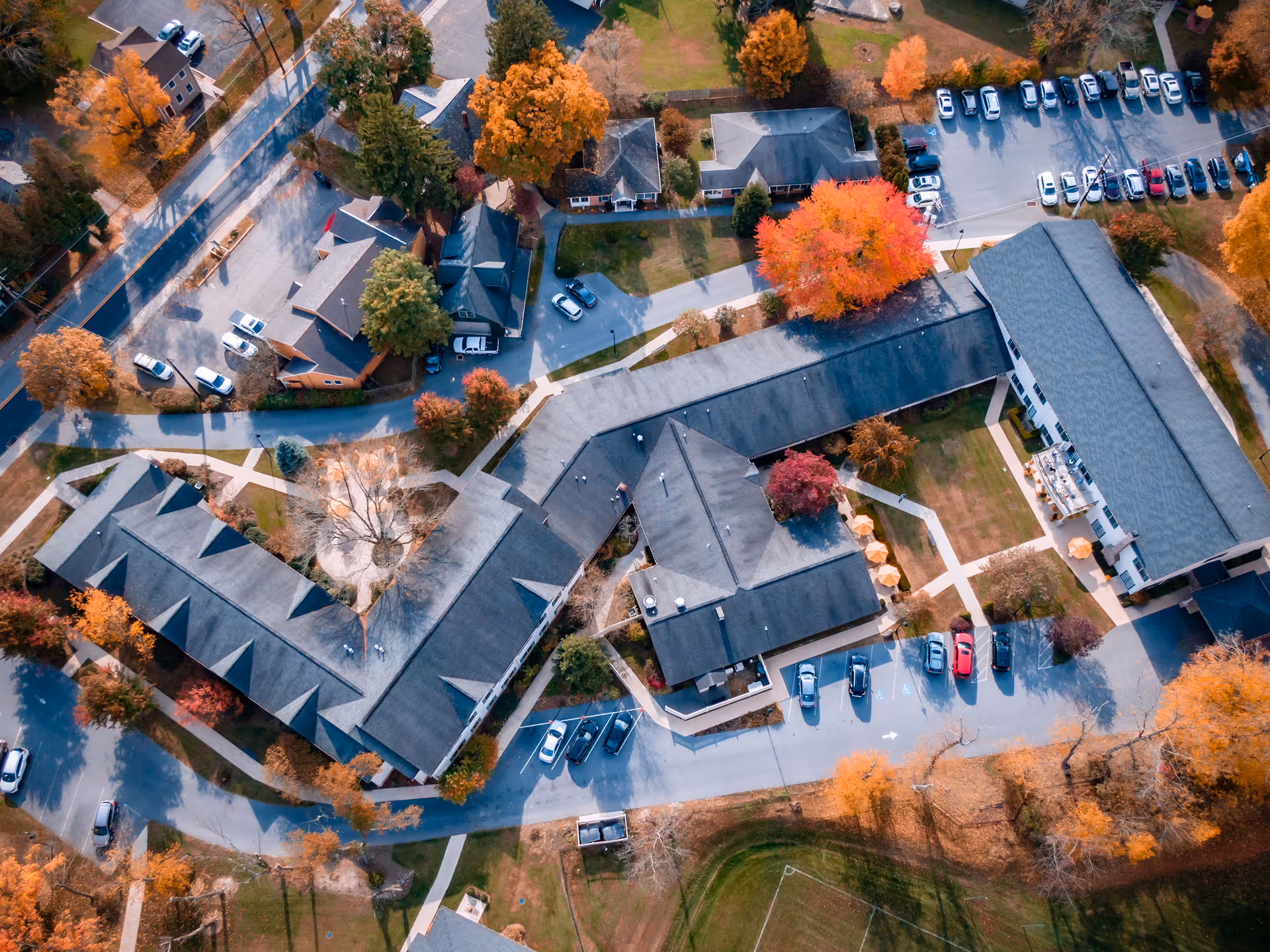 Aerial view of a senior living campus with interconnected buildings, parking areas, walkways, and trees in autumn colors.