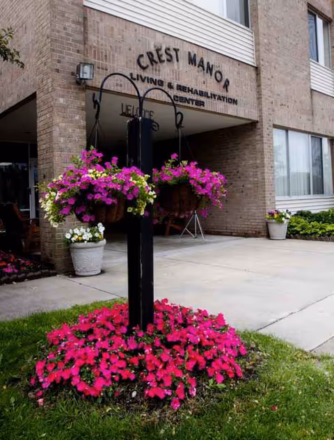 Exterior view of Crest Manor Living and Rehabilitation Center entrance with hanging flower baskets.