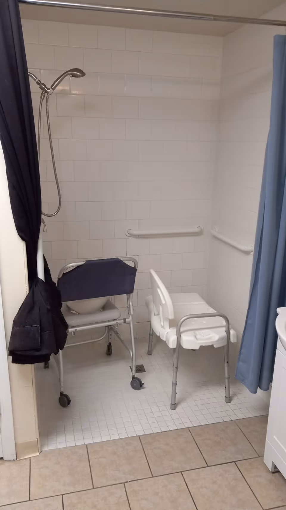 Accessible tiled shower with a handheld showerhead, grab bars, a commode chair and a shower chair.
