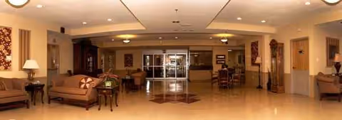 Spacious senior living facility lobby with sofas, lamps, and a central seating area.
