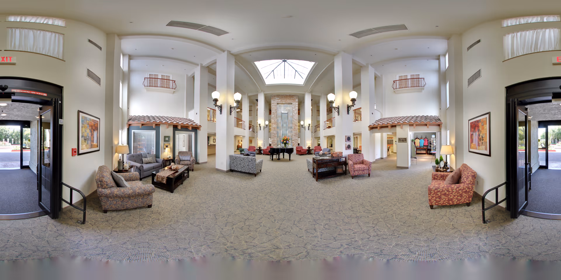 Spacious senior living facility lobby with high ceilings, a central skylight, multiple seating areas, and decorative columns.