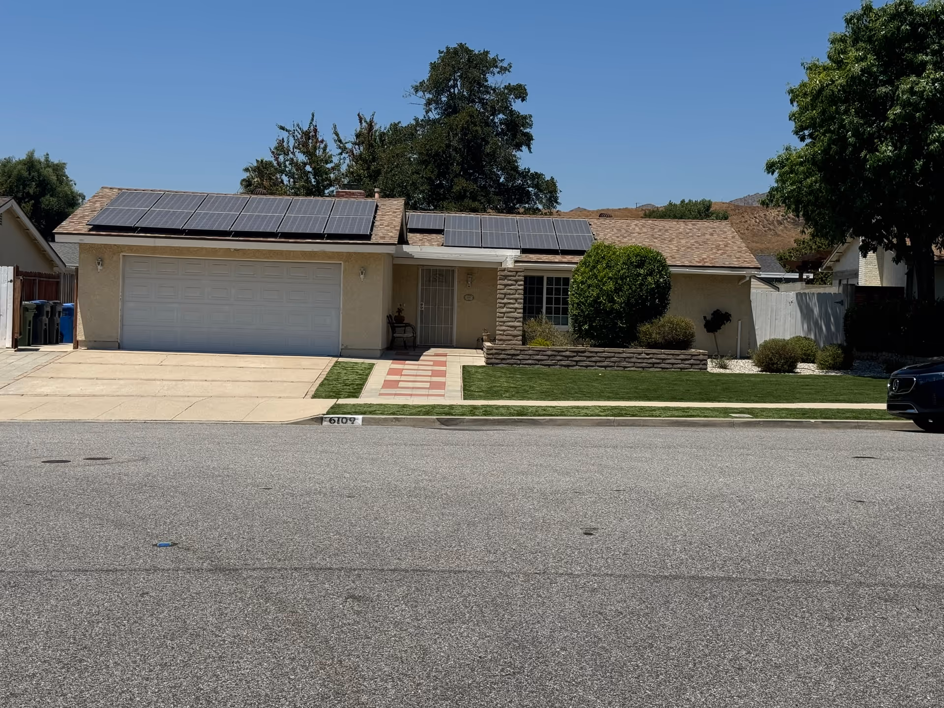 Single-story suburban house with a two-car garage, solar panels on the roof, driveway and front lawn.