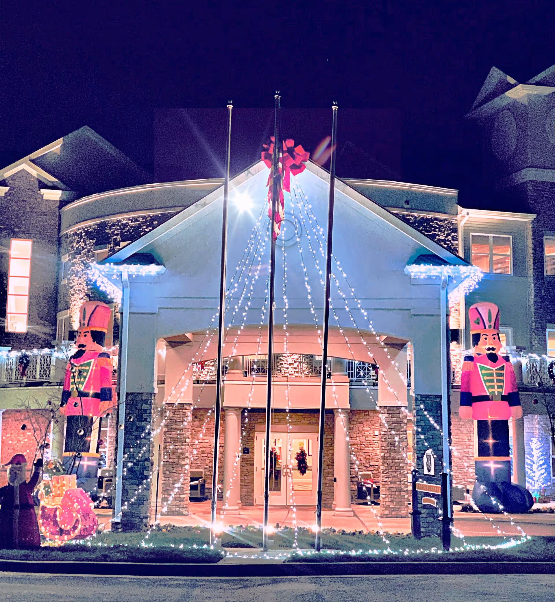 Night view of the entrance to Legacy Reserve at Fritz Farm decorated with holiday lights, including strings of white lights hanging from the roof, a large red bow at the peak, and two large inflatable nutcracker figures on either side of the entrance.