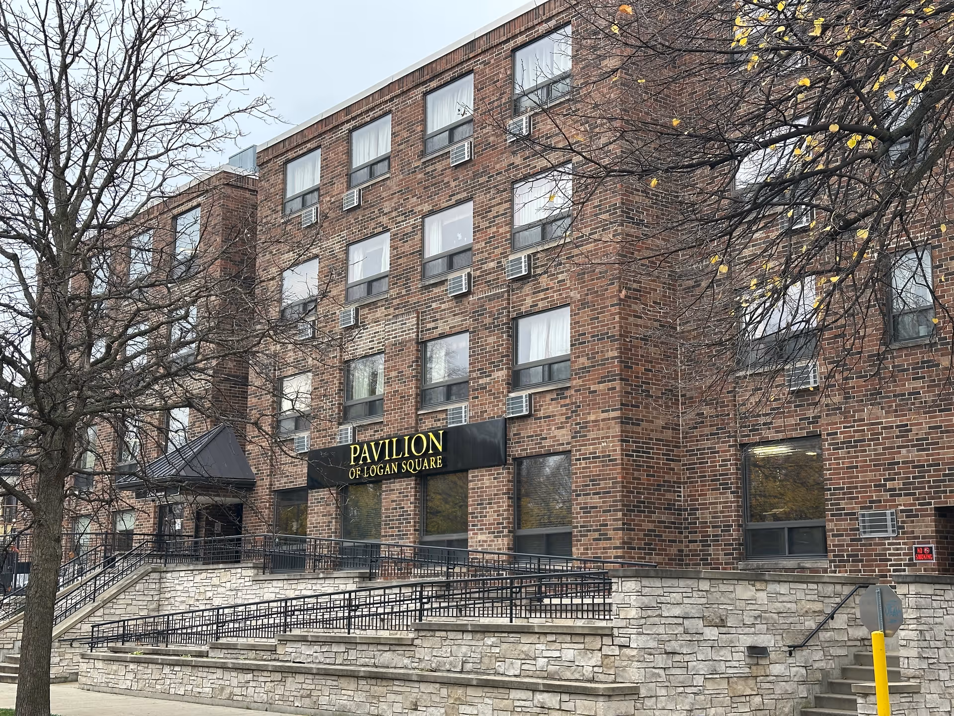 Front exterior of the Pavilion of Logan Square brick building showing the entrance, accessibility ramps, and the building sign.
