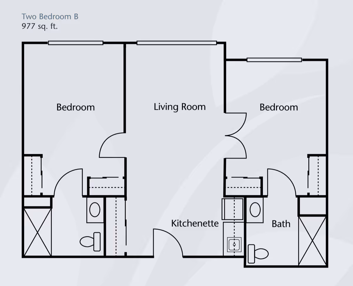 Floor plan of a two-bedroom apartment labeled 'Two Bedroom B' with 977 square feet. The layout includes two bedrooms, a living room, a kitchenette, and two bathrooms. Each bedroom has a closet, and each bathroom has a toilet and shower. The living room is centrally located with doors leading to both bedrooms and the kitchenette.